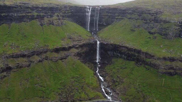 Cinematic aerial view of the giant Fossa waterfall cascading down green cliffs on a rainy day.