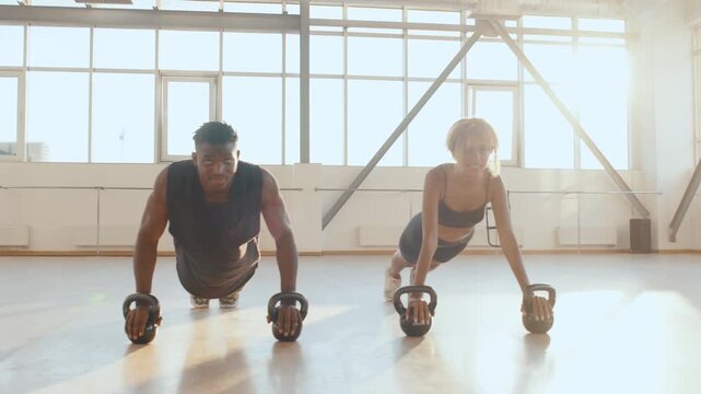 Afro fit couple perform kettlebell push-ups in a sunlit studio gym, demonstrating strength, balance and teamwork during an intense partner workout, Motivational fitness a health and lifestyle 4k
