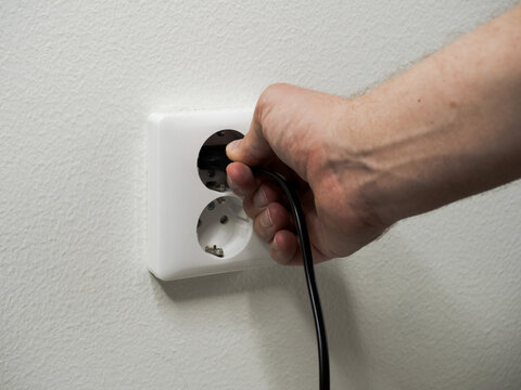 Hand plugging a black power cord into a white wall outlet. Energy, electricity and home concept.