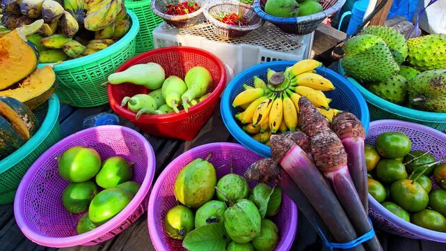 Top view of various organic tropical fruits and local vegetables arranged in colorful plastic baskets at a traditional outdoor market stall. 4K