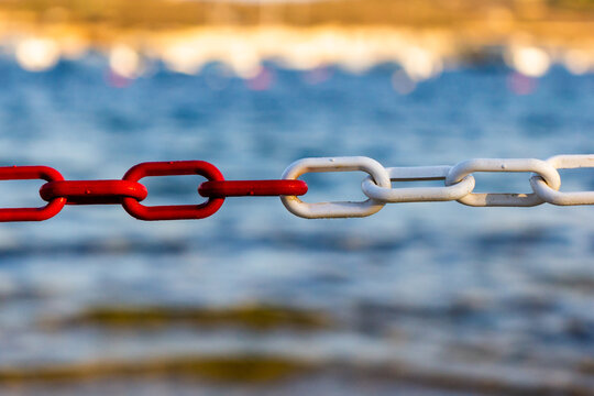 Red and White Chain Link by the Sea Symbolizing Connection, Contrast, and Nautical Boundary