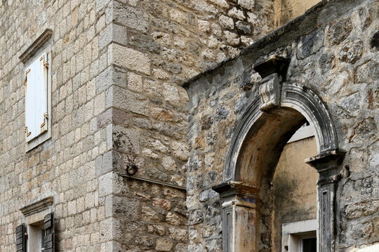 Old Mediterranean stone house facade with ancient archway and window shutters.