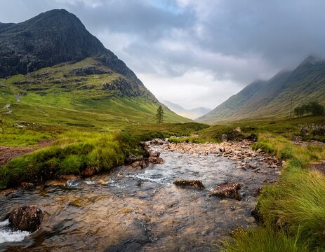 a stream flows through a valley in glen coe scotland mountains rise on either side under a cloudy misty sky in the scottish highlands