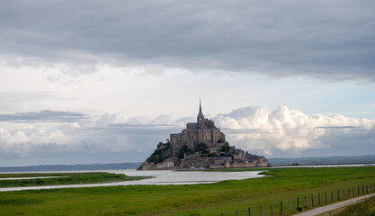 Road to Mont-Saint-Michel during high tide with rising water, tidal phenomenon on Atlantic's ocean coast, view on UNESCO heritage site and iconic Normandy landmark and green pastures © barmalini