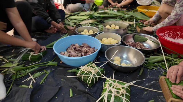 Vietnamese family making chung cake together for Tet holiday at home, Vietnam lunar new year, traditional food with ingredient sticky rice, mung beans, meat wrapping by green dong leaves