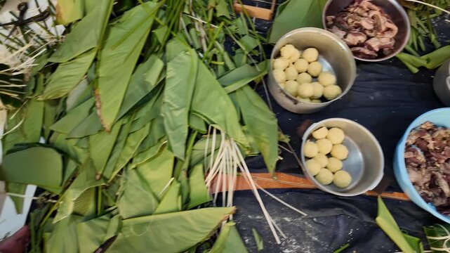 Vietnamese family making chung cake together for Tet holiday at home, Vietnam lunar new year, traditional food with ingredient sticky rice, mung beans, meat wrapping by green dong leaves