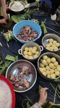 Vietnamese family making chung cake together for Tet holiday at home, Vietnam lunar new year, traditional food with ingredient sticky rice, mung beans, meat wrapping by green dong leaves