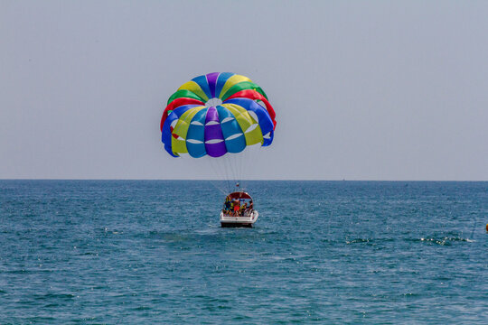 Horizontal eye level wide shot of a speedboat pulling a colorful parasail with tourists high above the sea on a bright sunny day