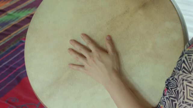 The hands of a girl touching shamanic drum with the wooden stick.