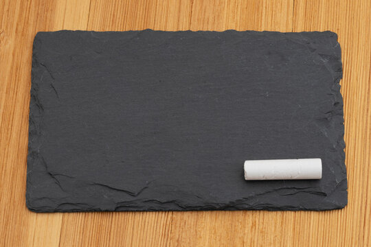 Blank chalkboard with a piece of chalk on a wood desk