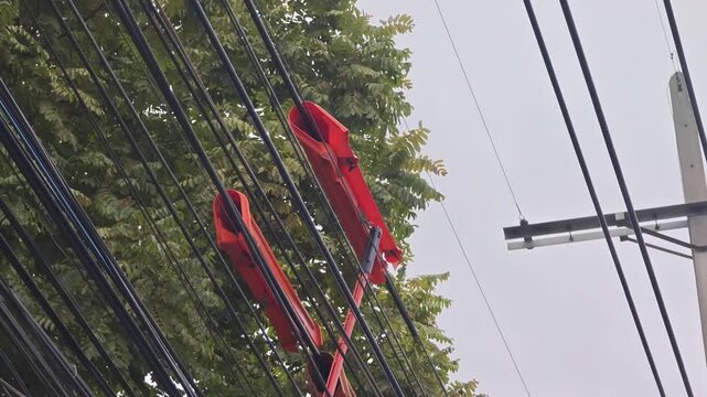 Video of sliding an orange insulated safety guard along high voltage overhead power lines near trees for trimming protection.