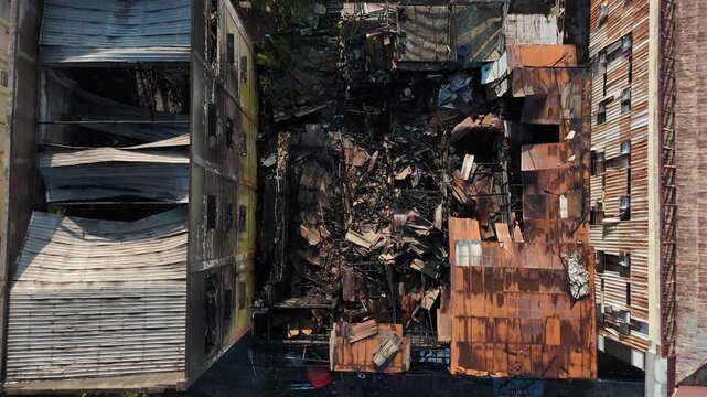An aerial view of urban buildings damaged by fire, rusted corrugated roofs, and collapsed structures.
