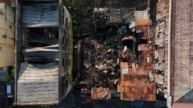 An aerial view of urban buildings damaged by fire, rusted corrugated roofs, and collapsed structures.