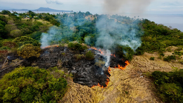Aerial view of a grassfire spreading across a tropical landscape. Thick smoke and advancing flames highlight wildfire risk, climate impact and environmental destruction.
