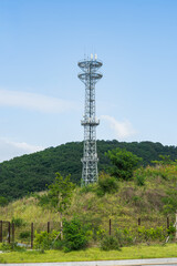 Obraz premium Telecommunication Tower on a Hill with Green Trees and Clear Blue Sky