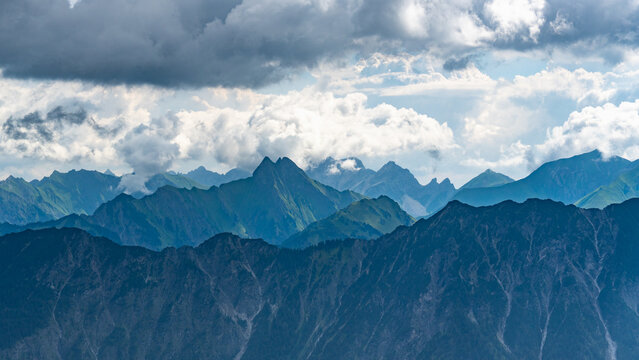 mountain range from little valley of Walser with green meadows and steep rocky slope in the alps of Bregenzerwald, with rocky mountains and steep, stony slopes on a rainy day with clouds.
