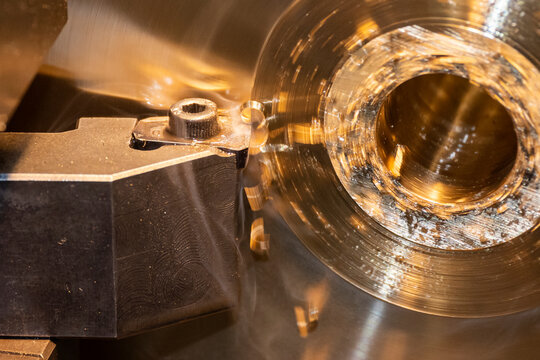 Macro shot of a lathe tool chip insert performing a cutting process on a brass material part.