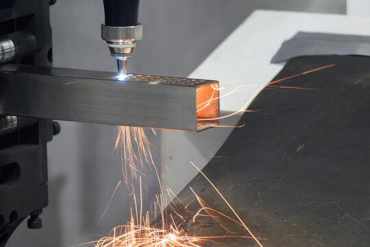 High-power fiber laser cut machine operation cutting a steel square pipe with a dramatic fire splash.