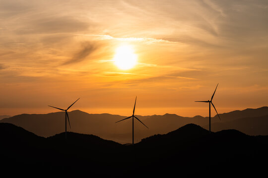 Wind Turbines Silhouetted Against a Golden Sunrise Over Misty Mountain Ridges, a Symbol of the Renewable Energy Transition