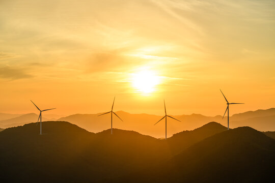 Wind Turbines Silhouetted Against a Golden Sunrise Over Misty Mountain Ridges, a Symbol of the Renewable Energy Transition