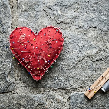 Heart Shaped Pincushion Covered in Pins on Stone Background