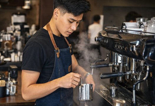 Professional barista working in a modern coffee shop steaming milk for a delicious latte drink
