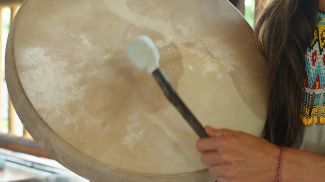 The hands of a girl playing a shamanic drum with the wooden stick.