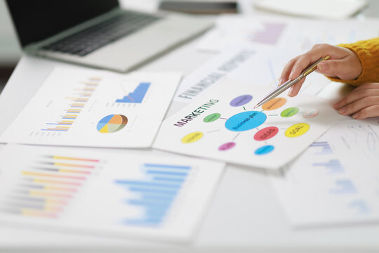 Business professional reviewing a mind map for a business plan, pointing at marketing concepts and analyzing financial reports, charts, and graphs on a white desk