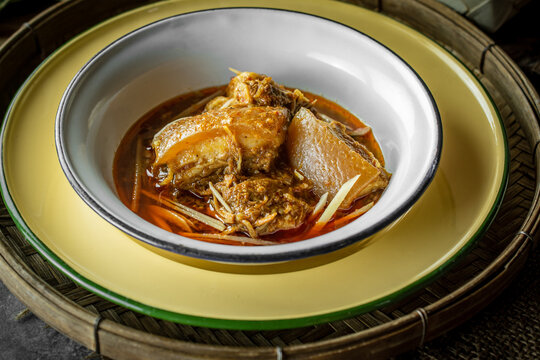 Traditional Northern Thai pork belly curry, known as Kaeng Hung Ley, served in a vintage yellow enamel bowl on a rustic bamboo tray, showcasing authentic Southeast Asian culinary heritage. 