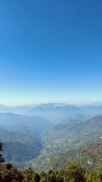 Aerial pan of misty mountain valleys terraced village. Green forests, clear blue sky for global travel tourism documentaries. Nature backgrounds adventure, vertical mount everest from Uttarakhand hill