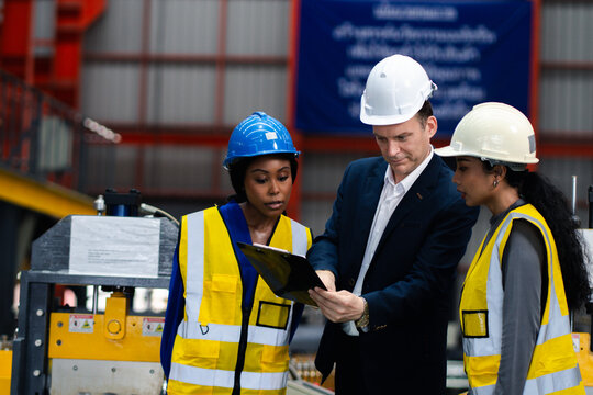 Industrial teamwork and digital manufacturing. Engineers review production data using a laptop and tablet beside factory machinery. Industry, teamwork, technology, inspection, production