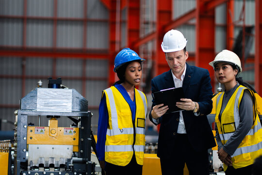 Industrial teamwork and digital manufacturing. Engineers review production data using a laptop and tablet beside factory machinery. Industry, teamwork, technology, inspection, production