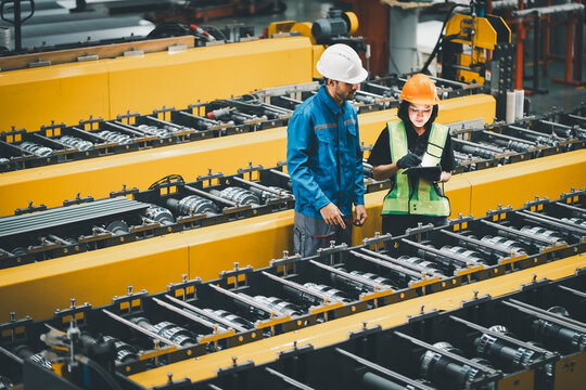 professional engineer,worker,technician use clipboard discuss work, walk in steel metal manufacture factory plant industry. Black African American man and woman wear hard hat check quality machine.
