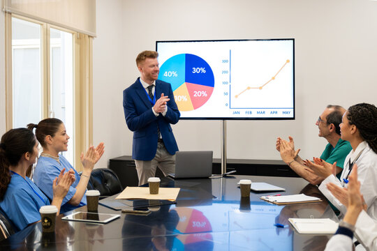 Medical team applauding a successful presenter during a business meeting with data charts