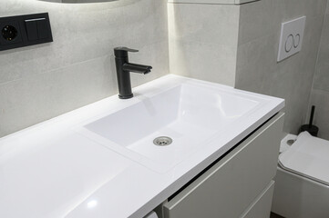Fototapeta premium modern bathroom features a white integrated sink with a matte black faucet, light‑gray tiles, a wall‑mounted toilet, sleek black power outlet for minimalist aesthetic