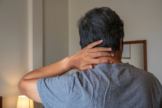 Middle-aged man with neck and occipital pain, standing indoors, medical healthcare and physiotherapy treatment concept.