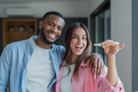 Smiling young couple embraces as the woman holds a key, celebrating buying and moving into their new home. Warm, joyful moment conveying homeownership, partnership and a fresh start together.