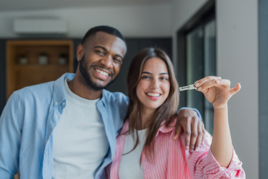 Interracial couple smiling at the camera, celebrating their real estate investment and holding the key to their new home, symbolizing financial achievement and a fresh start together
