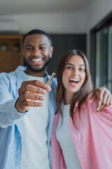 Fototapeta premium Diverse couple smiling, holding up a new key, celebrating their success and achievement of buying a home together, representing a new beginning and future