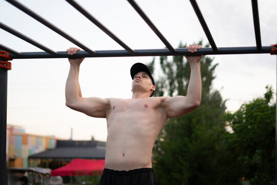 A man exercises on a pull-up bar in an outdoor gym at a park during late afternoon hours