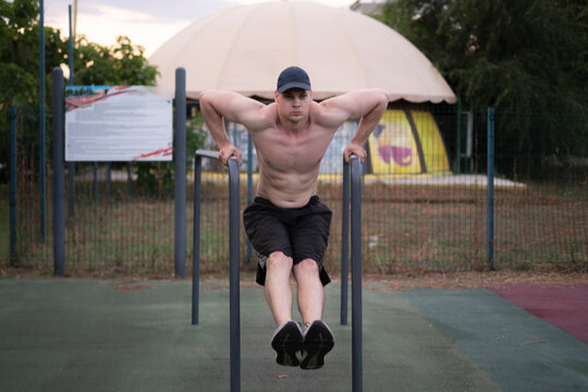 A man exercises on parallel bars in a park. It is late afternoon and the setting is quiet