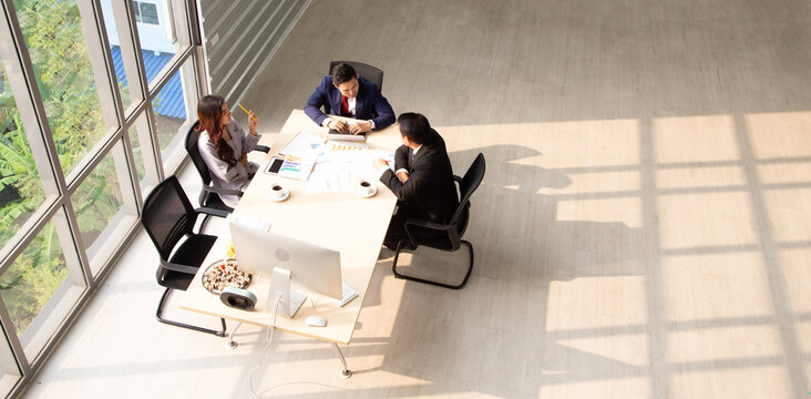 High-angle view of Asian business people having a meeting in a bright modern office. Professionals discussing financial charts and corporate strategy during a collaborative teamwork session