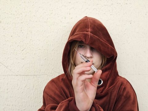 Portrait of a teenage child looking thoughtfully at a syringe with drugs