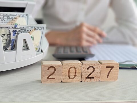 Planning finances for 2027 with cash, a calculator, and blocked numbers