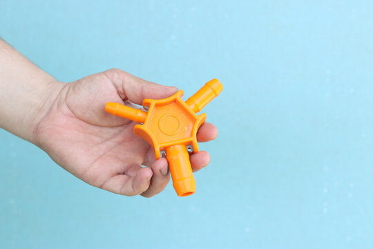 Male hand holds orange plastic star-shaped pipe calibrator. Tool for installing underfloor heating and plumbing on a blue background. Triple orange plastic calibrator for metal-plastic pipes