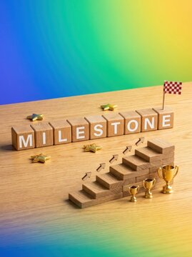 Wooden Blocks Spell Milestone with Stairs and Trophies Symbolizing Achievement.