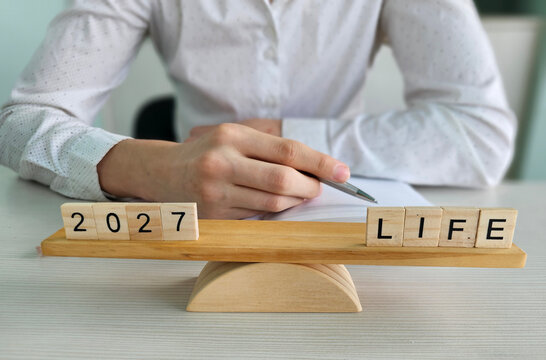 Person writes on paper with wooden blocks displaying 2027 and LIFE