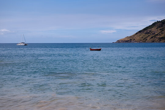 Tropical beach view with incoming waves on the sand and a lush green island coastline under cloudy sky
