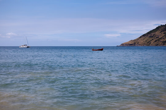 Tropical beach view with incoming waves on the sand and a lush green island coastline under cloudy sky