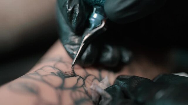 Close up of a professional tattoo artist using a tattoo machine to create a detailed design on a client arm in a tattoo studio.